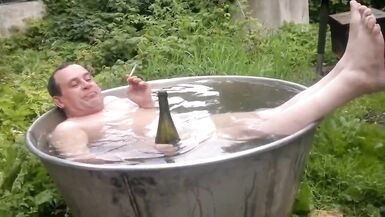 Nude old guy rolls around in outside bathroom tub.